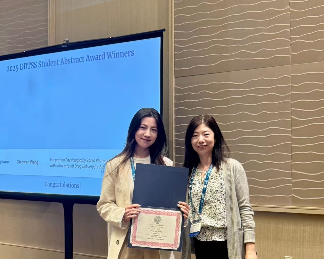 Xiaowen Wang holding her award certificate beside the award presentation screen.